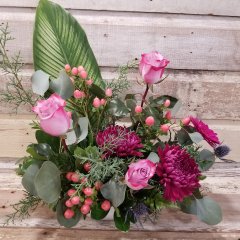 Flower Arrangement/Floral Bouquet - Pink Roses, Berries and Mums with Sea Holly/Blue Thistle. Large Aspidistra leaf with Eucalyptus and other greenery. In a white Boat shaped ceramic container