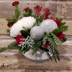 Flower arrangment for christmas with wintergreens red and white flowers in a white ceramic container with silver orrnaments